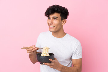 Young Argentinian man over isolated white background holding a bowl of noodles with chopsticks