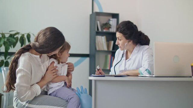 Female Family Doctor Examining and Consulting to Mother and Her Child. Mother With Kid at Visiting Pediatrician. Talking With a Doctor At Consultation During an Appointment.