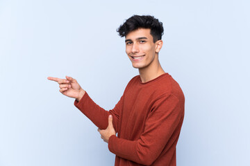 Young Argentinian man over isolated blue background pointing finger to the side