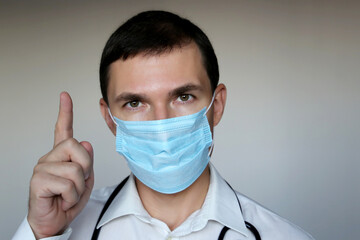 Doctor in disposable face mask points up. Concept of coronavirus protection