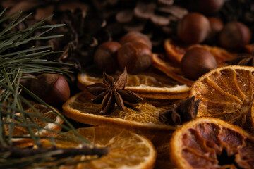 Christmas background with pine tree branches, hazelnuts, anise stars and dried orange on dark board. Christmas decorations. 