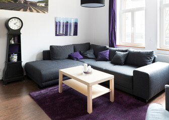small living room with clock and grey sofa and lavender pictures