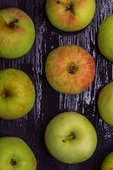 View from above of the small fresh apples that lie on a black wet wooden background