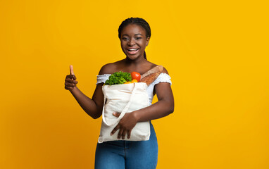 Smiling african american woman holding bag with groceries and showing thumb up