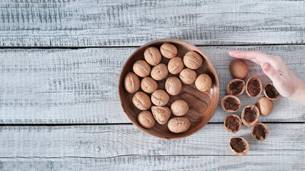 On a wooden background, a wooden plate with walnuts and the hand sweeps the shell next to it.