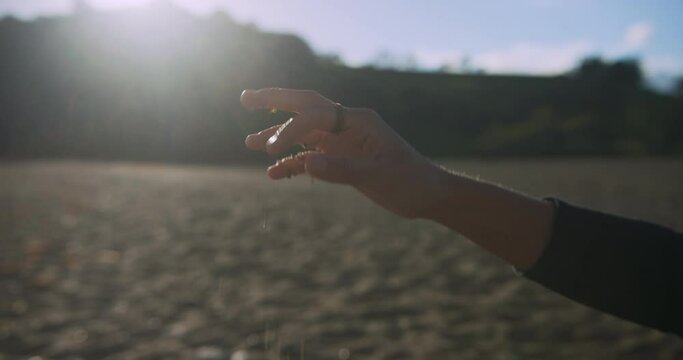 The hand of a young woman is dropping a handful of pebbles on the beach