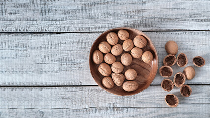 On a wooden background, a wooden plate with walnuts and a shell next to it