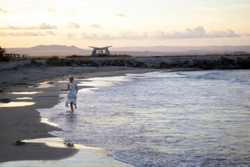 Happy girl in white bathing suit. girl walking along the beach. Girl on the shore of the ocean.