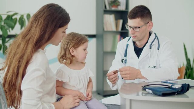 Male Doctor Pediatrician Giving Some Tablets for Ill Kid. Mother With Kid at Visiting Pediatrician. Talking With a Doctor at Consultation During an Appointment.