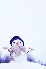 Little snowman in a hat and scarf on the snow on a winter day, soft selective focus, copy space. Christmas background, winter holidays, preparation for the holiday