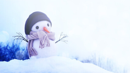 Little snowman in a hat and scarf on the snow on a winter day, soft selective focus, copy space. Christmas background banner, winter holidays, preparation for the holiday