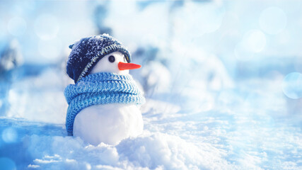 Little snowman in a hat and scarf on the snow on a sunny winter day, soft selective focus, copy...