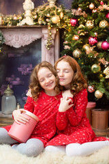 Obraz na płótnie Canvas two red-haired sisters near the New Year tree. Christmas holiday atmosphere, lights, gifts, smiles