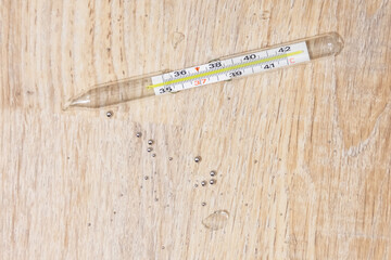Randomly broken medical thermometer to measure a person's body temperature, glass fragments and drops of dangerous mercury on the floor.