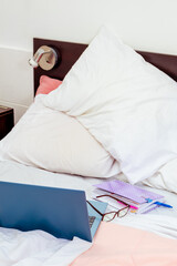 Open laptop, diary and glasses on a bed in a bedroom. I work from home, comfortable form of communication or entertainment. Current concept of work from home.