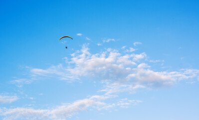 Paraglider flying against blue sky with clouds in middle at sunny daylight