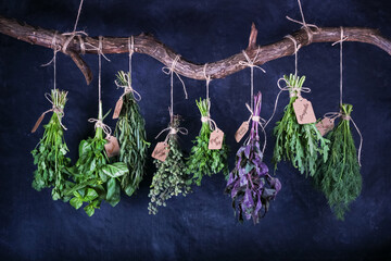 Hanging bunches of edible herbs with signed tags on a curved wooden crossbar, closeup on black...