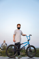 Obraz premium Portrait of a teenager in the sunset in a black mask on a blue bicycle. Quarantine. It is forbidden to ride a bicycle. Covid-19.