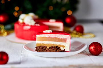 Mousse Christmas pastry cake dessert covered with red mirror glaze with new year decorations on garland lamps bokeh white background, Modern european cake Christmas theme. .
