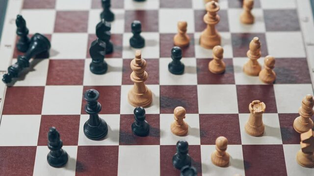 Black king chess piece gets knocked over by the white king chess piece, black team has been defeated.