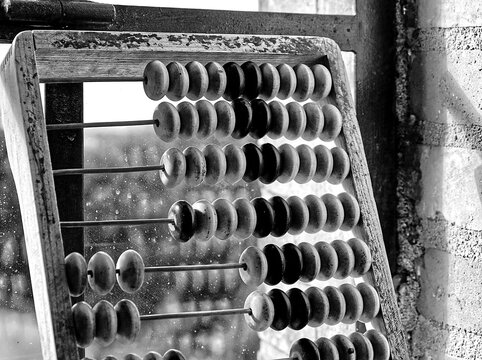 Black and white photography of an abacus lying against a window.