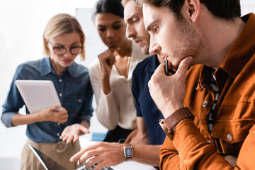 thoughtful multiethnic businesspeople pointing with hands at laptop while thinking together on...