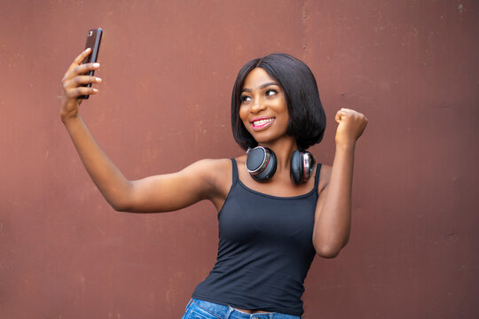 image of beautiful young african lady, excited black girl, with  head phone, smart phone- music concept 