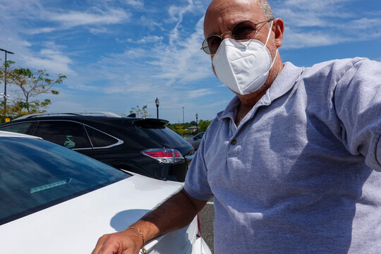 A Mature Bald Caucasian Man Wearing A White Face Mask With His Arm On The Trunk Of A White Car