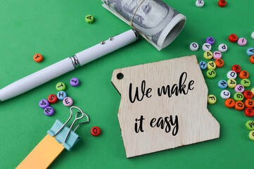 Selective focus of alphabet beads, banknote, pen, sticky note and wooden board written with text WE MAKE IT EASY. Business and education concept.