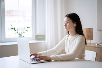 Cute teenager girl sitting at table and doing homework. Education concept, distance learning, self-education, video conference class with tutor    