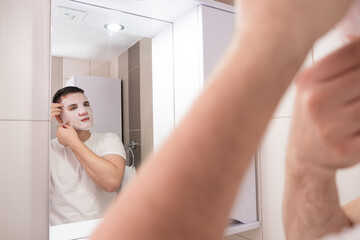 reflection in the mirror man takes care of his face. guy in the bathroom with a face mask