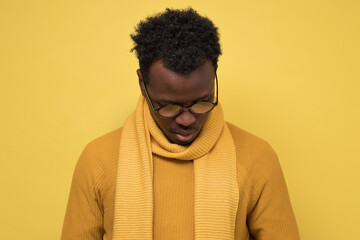 Fototapeta premium Young distressed african man wearing glasses looking down. Studio shot on yellow wall.
