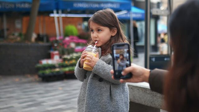 Happy little girl adorably sipping a yellow smoothie while she is recorded