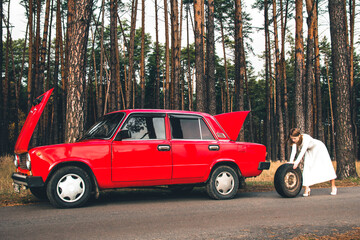 Girl in a wedding dress rolls the wheel. Vaz 2101. Red retro car in the forest