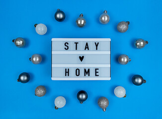 Light box with stay home quote on a blue background with Christmas balls.