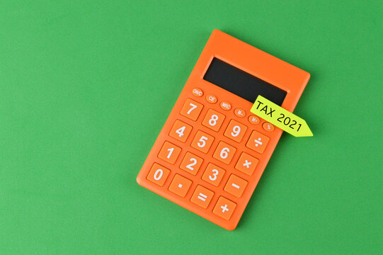 Top view of calculator and sticky note written with TAX 2021 on a green background. Business concept. Copy space for text.