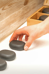 Hand of masseur lays out massage stones on the table in spa salon