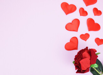 Artificial red rose bud and decorative hearts on a pink background with a copy space. Valentine's day concept.