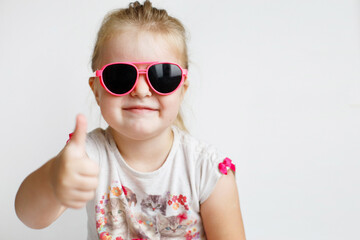 Child in pink sunglasses making funny face and smiling. positive girl thumbs up on a white background