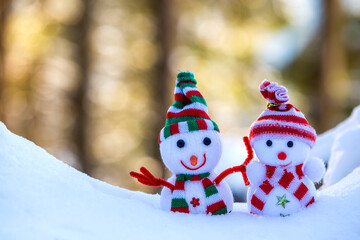 Two small funny toys baby snowman in knitted hats and scarves in deep snow outdoors on bright blue and white copy space background. Happy New Year and Merry Christmas greeting card.