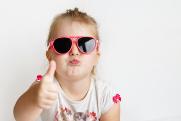 Child in pink sunglasses making funny face. positive girl thumbs up on a white background