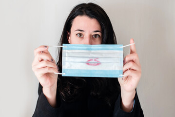 Una mujer joven morena sujeta una mascarilla quirúrgica azul manchada de pintalabios 