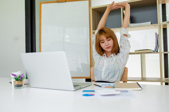 A female finance worker is stretching her arms to relax as she works hard overtime to relax during work. In her office, the concept of relaxation at work