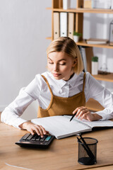 young, focused accountant working with calculator near blank notebook