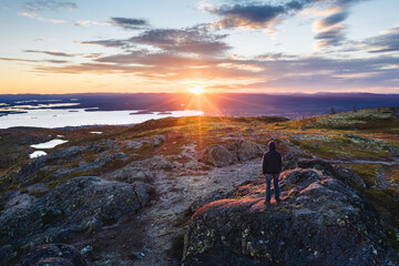 Single man on rock top in mountain tundra landscape at sunset. Outdoor and hiking background. Northern nature scenery near Kandalaksha. Kola Peninsula, Murmansk Oblast, Russia