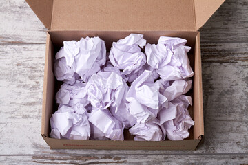 Crumpled paper balls filler in cardboard box. Opened parcel with filler on wooden floor.