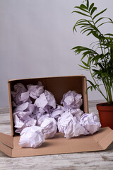 Crumpled paper balls filler in cardboard box. Opened parcel with filler on wooden floor. Green houseplant on the rustic wooden floor.