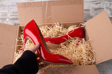 Wobox's hand is holding a red shoe. Shiny red stilettos in the open parcel with wood shavings...