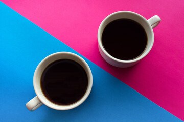 Obraz na płótnie Canvas Two coffee cups on wooden saucers against pink and blue diagonally divided background. Coffee together concept. Tea for lovers couple