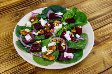 Tasty spinach salad with boiled beetroot, feta cheese, walnut and red onion on wooden table. Healthy vegetarian food